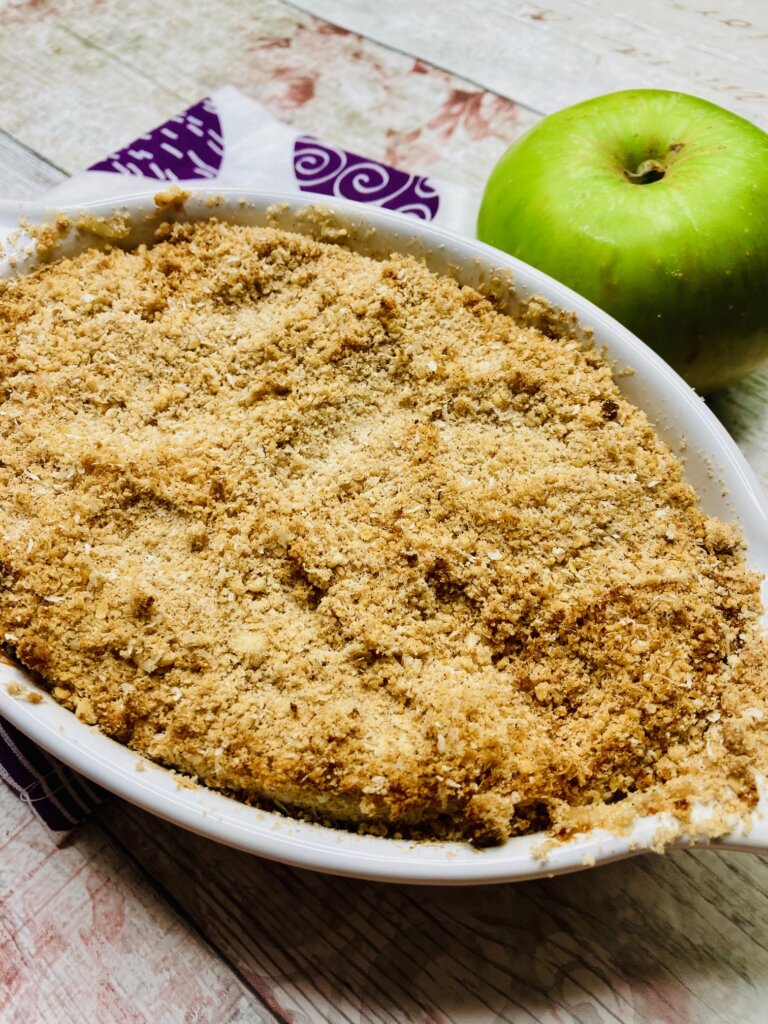 Cooked apple crumble for two in a white dish with an apple in the background